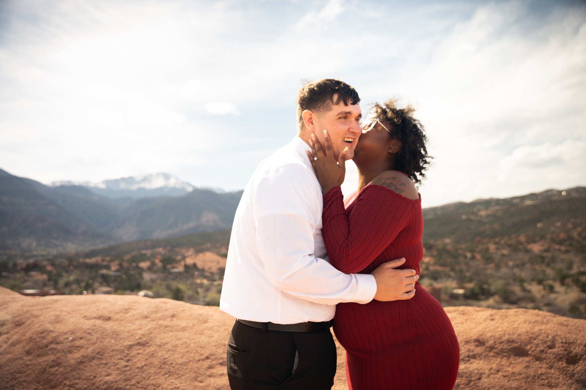 Playful engagement portrait with a kiss against the mountain landscape