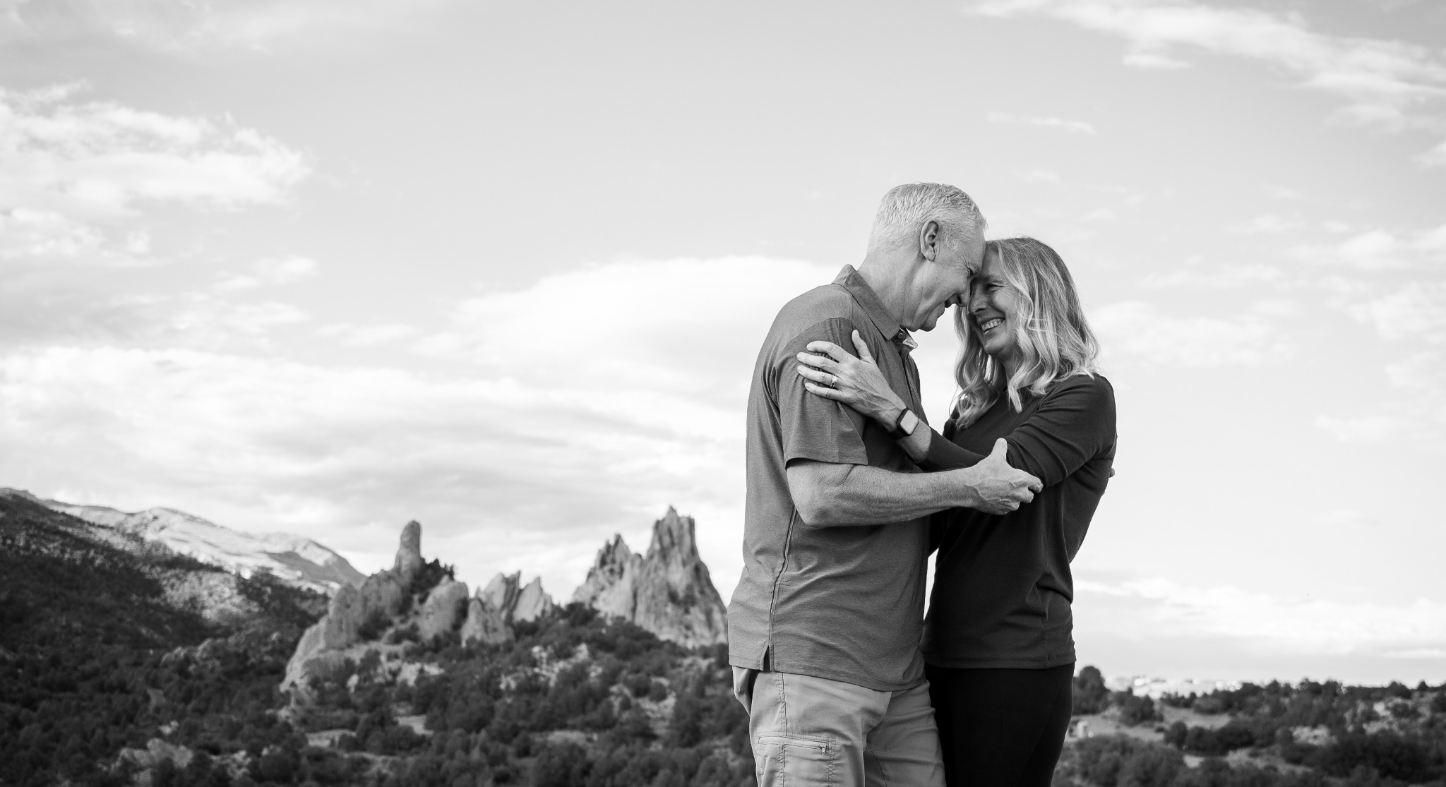 Couple embracing with the Garden of the Gods rock formations behind them in black and white
