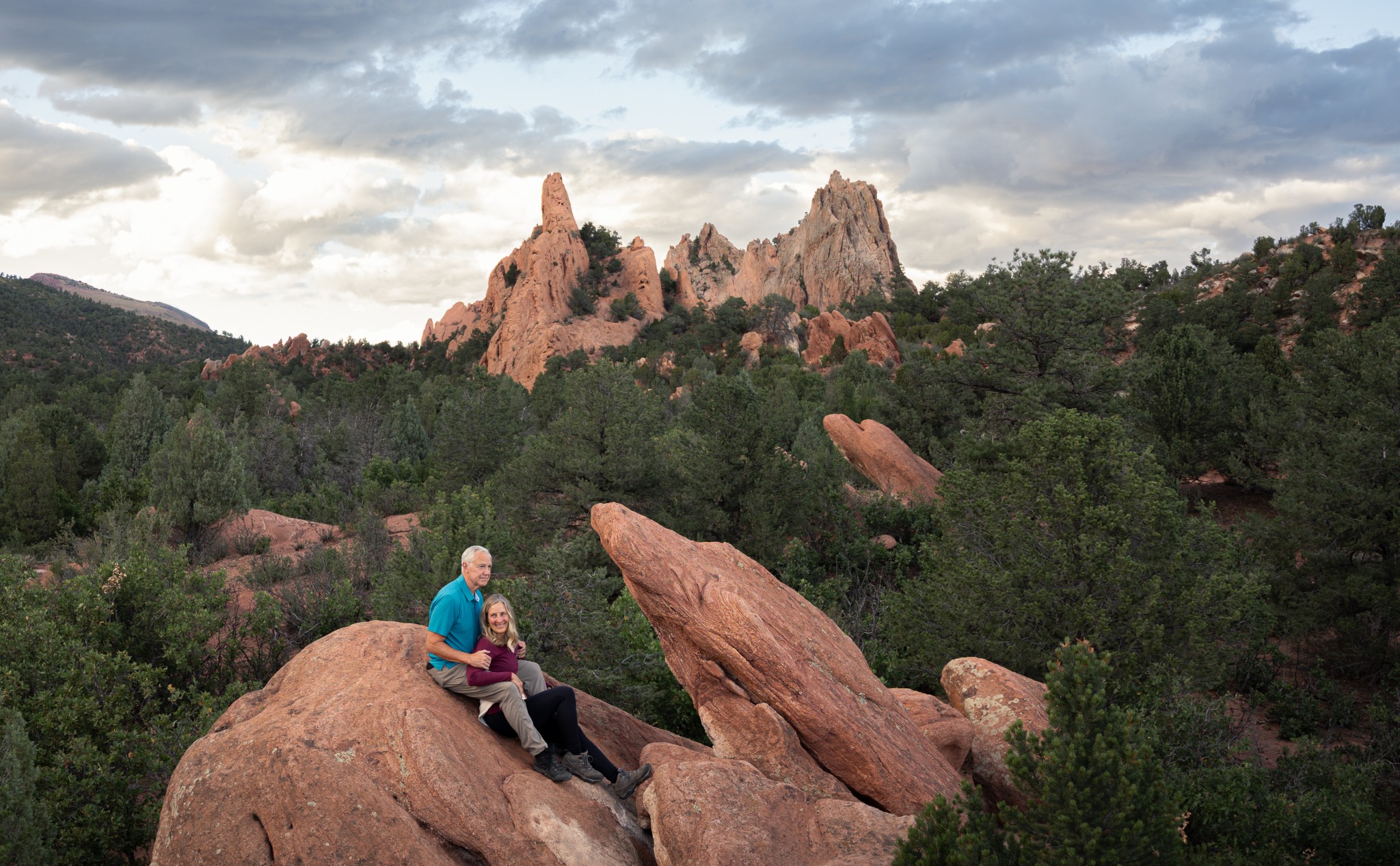 Couple resting together on red rocks beneath a dramatic Colorado sky